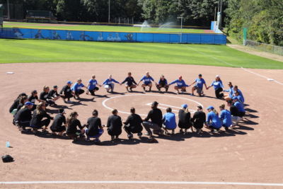 Alumni Softball players huddle up in a circle around the mound