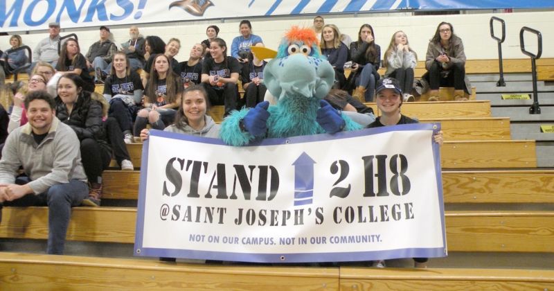 The College's character "Blue" holds a sign for NOH8 at a basketball game.