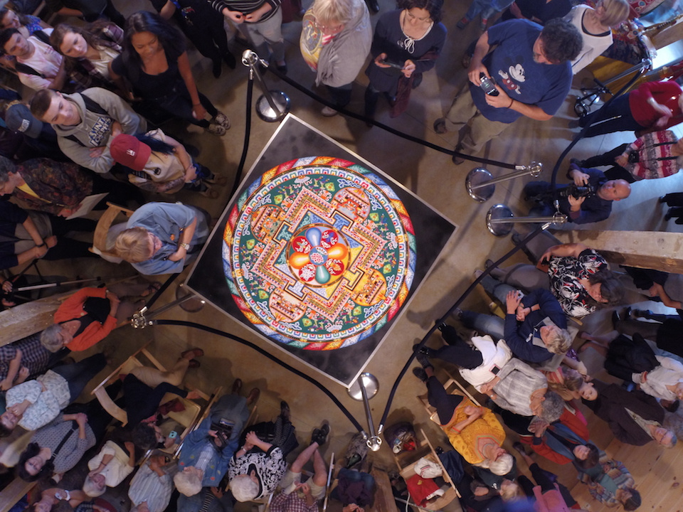 A crowd of people look at a colorful mandala painting