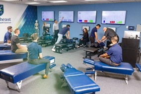 A group of individuals participate in a chiropractic training session at Saint Joseph’s College. Trainers from the Sciences Department demonstrate techniques on chiropractic tables, while others observe monitors displaying data as part of the Doctor of Chiropractic Program. Saint Joseph's College of Maine