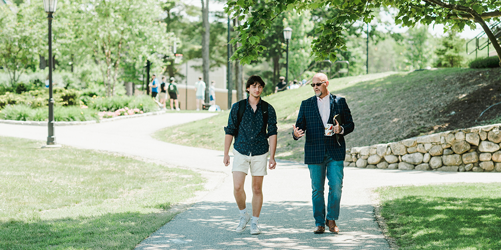 Professor and student talk while walking across campus together