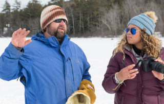 Professor Scott Fuller instructs a photography student during an outside digital photography class on a frozen Sebago Lake.